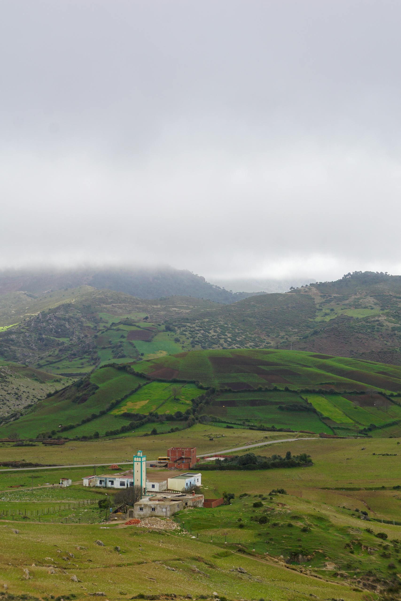 Vivid landscape featuring lush hills, a rural building, and a cloudy sky, capturing the essence of serene countryside life.